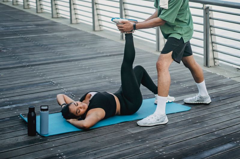 Woman stretching outdoors, assisted by a trainer